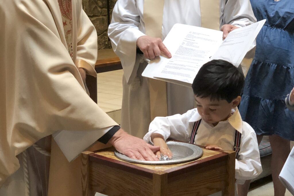 Child and priest with hands in baptismal water